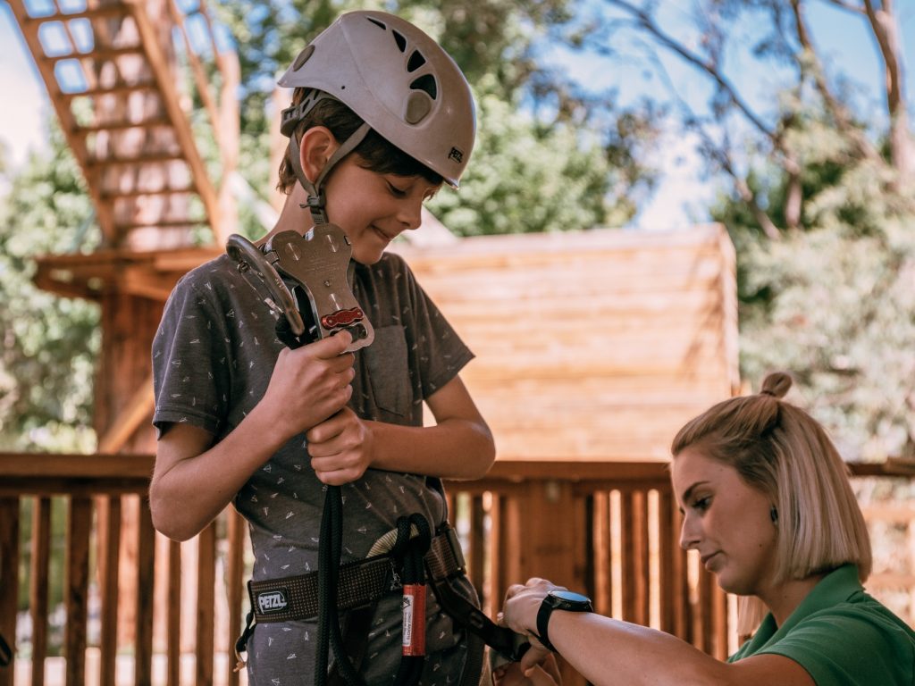 A teen getting ready for the Grand Tree Surfing at Enchanted Adventure with one of our instructors securing the harness
