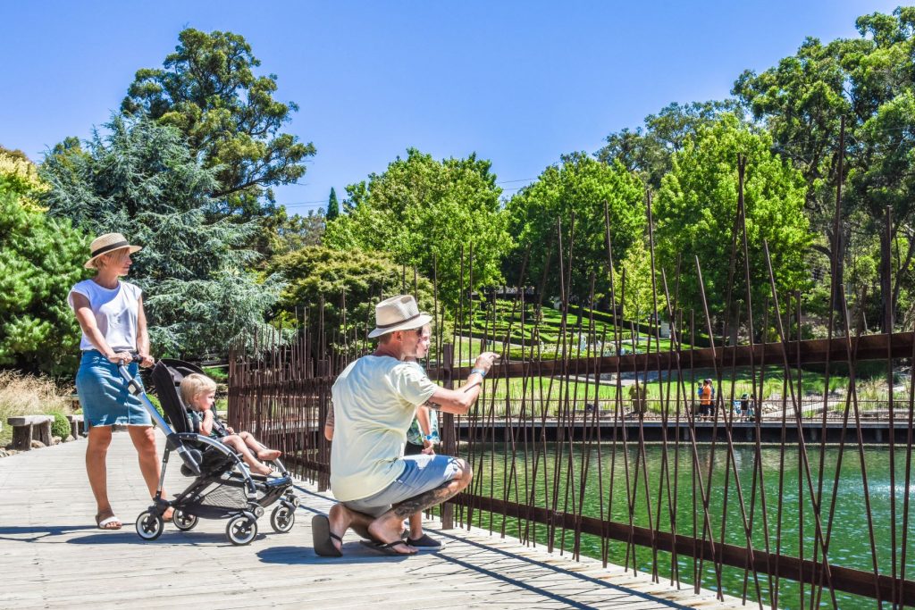 Family with pram on a boardwalk overlooking lake with formal gardens in background
