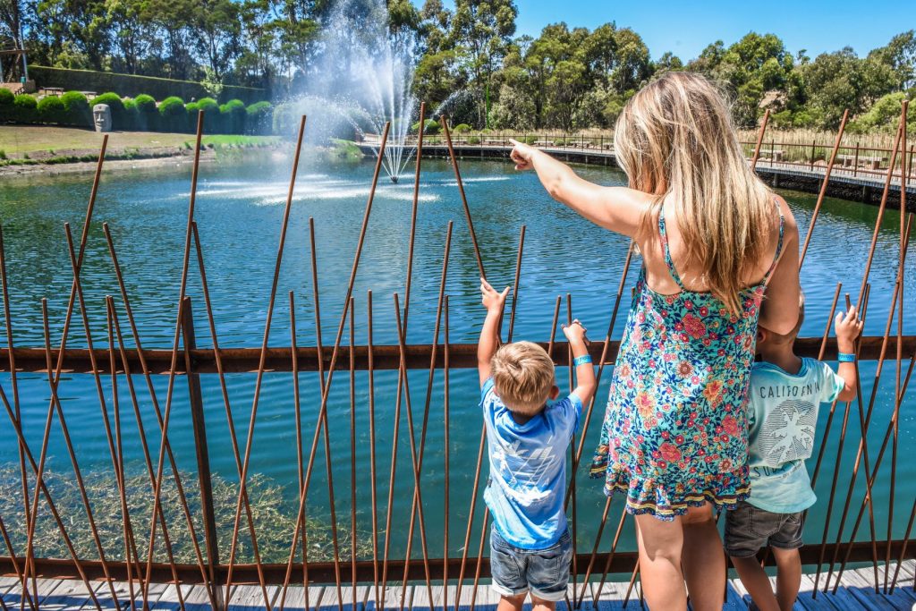 Mum and two small children exploring and pointing out sculptures around the Enchanted Lake in summer