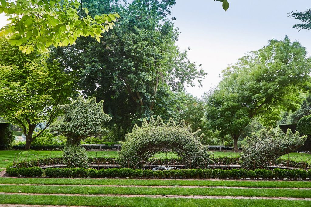 Hedge Sculpture of Loch Ness serpent set in a pond with lush trees in the background